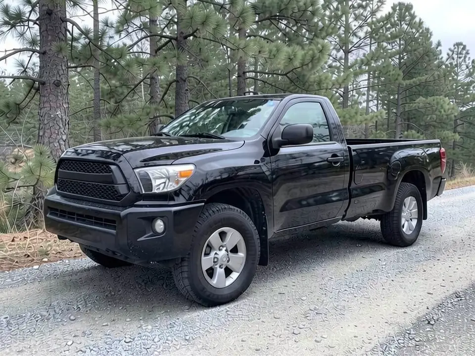 AI-drawn sample: a black Tacoma-style regular cab pickup with an empty bed and silver wheels on a gravel road beside pine trees